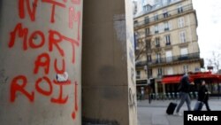 Orang-orang berjalan melewati grafiti bertuliskan "Matilah Sang Raja" sehari setelah bentrokan selama aksi protes atas reformasi pensiun pemerintah Prancis di Paris, 24 Maret 2023.