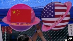 Seorang penjual menyiapkan makanan dan minuman di sebuah gerai yang menampilkan bendera-bendera China dan Amerika yang berbentuk planet selama Karnaval Musim Semi di Beijing pada 13 Mei 2023. (Foto: AP)