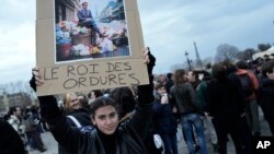 Seorang perempuan mengangkat plakat bertuliskan "raja sampah" bergambar Presiden Prancis Emmanuel Macron duduk di tong sampah, selama aksi protes menentang reformasi pensiun, di Paris, Prancis. 
