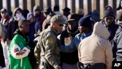 A member of US Customs and Border Protection tries to control a group of migrants as hundreds gather along the border after breaking through gaps in the border wall Dec. 5, 2023, in Lukeville, Ariz. 