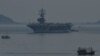 A fishing boat (R) sails past the USS Ronald Reagan, a U.S. Navy Nimitz-class nuclear-powered aircraft carrier, in Danang, Vietnam, June 25, 2023. 