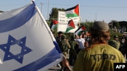 FILE - Pasukan keamanan Israel berdiri di antara pemukim Yahudi dan warga Palestina ditemani oleh aktivis Israel dan asing, masing-masing pihak membawa bendera nasional mereka, di sebelah timur kota Qalqiliya di Tepi Barat yang diduduki, 9 Mei 2022. (JAAFAR ASHTIYEH/AFP)