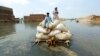 FILE - Flood victims use a makeshift barge to carry hay for cattle, in Jaffarabad, a district of Pakistan's southwestern Baluchistan province, on Sept. 5, 2022.