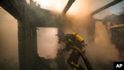 Petugas pemadam kebakaran Ukraina berusaha memadamkan api pada sebuah rumah yang hancur akibat terkena serangan Rusia di Kyiv, Ukraina, pada 23 Maret 2022. (Foto: AP/Vadim Ghirda)