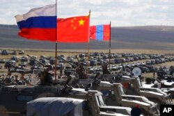 Bendera nasional Rusia, Cina, dan Mongolia yang dipasang pada kendaraan lapis baja berkibar tertiup angin selama latihan militer di tempat latihan "Tsugol", sekitar 250 kilometer tenggara kota Chita selama latihan militer Vostok 2018 di Siberia Timur, Rusia, Kamis , 13 September 2018. (Foto: AP)