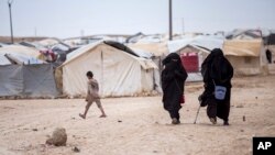 FILE - Women walk in the al-Hol camp that today houses about 51,000 people, the vast majority women and children, including the wives, widows and other family members of IS militants, in Hasakeh province, Syria, May 1, 2021.