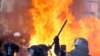 Flames from a fire rise behind law enforcement officers during a demonstration against the French government's pension reform plan as part of the fourth day of national protests, in Paris, France, Feb. 11, 2023.