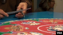 Mandala artist Losang Samten is dispensing sand using metal tools called Chakpur, which he has been using for more than 30 years to create mandalas. (VOA/ J. Soh)