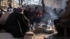 People sit around fire as they are surrounded by debris, following the deadly earthquake in Maras, Turkey, Feb. 11, 2023. In the aftermath of the quake, looters have been stealing from shops and cars.