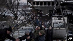 Warga Ukraina melintasi jalur improvisasi di bawah jembatan yang hancur saat melarikan diri dari Irpin, di pinggiran Kyiv, Ukraina, Selasa, 8 Maret 2022. (Foto: AP/Felipe Dana)