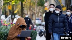 Seorang wanita yang mengenakan masker melihat laptopnya di jalan, saat wabah COVID-19 masih terus terjadi di Shanghai, China, 14 Desember 2022. (Foto: Reuters)