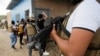 FILE - A member of Honduras' Police Anti Maras and Gangs Against Organized Crime Directorate stands guard as other directorate members frisk people in Tegucigalpa, Honduras, Nov. 26, 2022. 