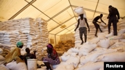 FILE: Men carry bags of food while women wait for their rations at the United Nations World Food Programme (WFP) food distribution site in Pibor, South Sudan, June 25, 2012.