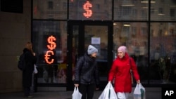 Dua perempuan berjalan melewati kantor penukaran uang yang menampilkan nilai tukar antara dolar dan euro dengan rubel pada layar kantornya di Moskow, Rusia, pada 1 April 2022. (Foto: AP)