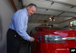 Jeff Solie sedang mengisi baterai mobil sedan listrik Tesla di rumahnya di New Berlin, 13 Juli 2017.