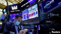 Seorang pialang saham tampak sibuk bekerja di saat layar di belakangnya menampilkan pidato dari Kepala Bank Sentral AS Jerome Powell, di Kantor Bursa Saham New York, pada 26 Januari 2022. (Foto: Reuters/Brendan McDermid)