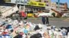 People walk past piled up garbage as trucks block a highway during a protest by Land Transport Unions against worsening economic conditions, in Dora, Lebanon Feb. 2, 2022. 