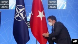Seorang petugas membetulkan letak bendera Turki yang berdampingan dengan bendera NATO pada KTT NATO di Brussels, 14 Juni 2021. (Foto: via AP)