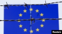 Kawat berduri di depan bendera Uni Eropa di sebuah pusat penerimaan imigrasi di Bicske, Hungaria (25/6). (Reuters/Laszlo Balogh) 
