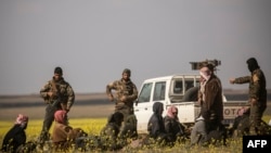 U.S.-backed Syrian Democratic Forces stand guard over men suspected of being Islamic State (IS) group fighters at a screening point outside Baghuz in eastern Syria, March 6, 2019.