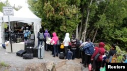A line of asylum-seekers who said they were from Haiti wait to enter into Canada from Roxham Road in Champlain, New York, Aug. 7, 2017.