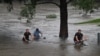 Orang-orang mengendarai sepeda melalui sebuah taman yang tergenang banjir di tepi sungai Nepean di pinggiran Penrith, saat kota Sydney, Australia, bersiap menghadapi banjir terburuk dalam beberapa dekade, Minggu 21/3. (Foto: AFP)