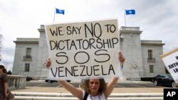 Yon manifestan kap pwoteste kont rejim Prezidan Nicolas Maduro a, kenbe anlè yon ansèy ki ekri, "nou di non ak diktati o Venezuela" devan building OEA, nan Washington kote yon rankont tap dewoule sou kriz venezuelyèn nan jedi 24 janvye 2019 la. 