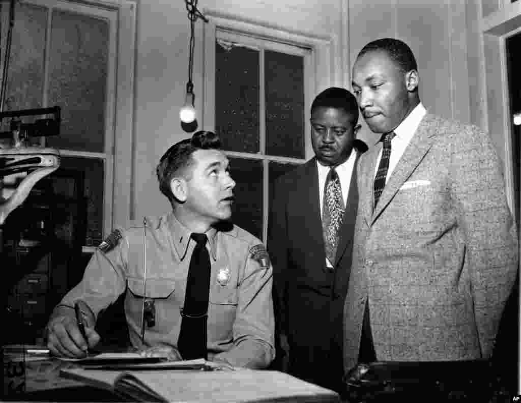 1956 - A ranar 23 Fabrairu 1956, Martin Luther King, Jr., tare da Rev. Ralph D. Abernathy sun mika kawunansu ga jami&#39;in &#39;yan sanda Lt. D.H. Lackey a Montgomery, Jihar Alabama, bayan da aka tuhume su da haddasa yamutsi dangane da gangamin kauracewa shiga bas-bas na birnin.