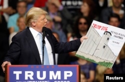 U.S. Republican presidential candidate Donald Trump holds a sign supporting his plan to build a wall between the United States and Mexico that he borrowed from a member of the audience at his campaign rally in Fayetteville, North Carolina.