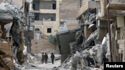 FILE - Fighters from Syrian Democratic Forces walk together along a damaged street in Raqqa, Syria, Sept. 16, 2017. The unidentified American being held in Iraq as an enemy combatant was captured in Syria in September by the SDF.