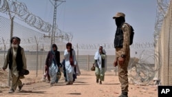 FILE - In this Aug. 20, 2021, photo, Pakistani army soldier stands guard while Afghan people enter into Pakistan through a border crossing point, in Chaman, Pakistan.