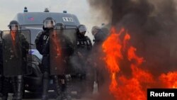 Polisi Prancis dan polisi anti huru hara CRS berdiri di dekat api ketika para demonstran berkumpul di Place de la Concorde dekat Majelis Nasional di Paris, Prancis, 16 Maret 2023. (Foto: REUTERS/Lucien Libert)
