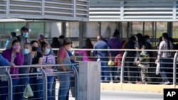 Travelers, left, waiting in line to cross a customs area into the United States at the McAllen-Hidalgo International Bridge look on as a group of migrants, right, are deported to Reynosa, Mexico, March 18, 2021, in Hidalgo, Texas. 