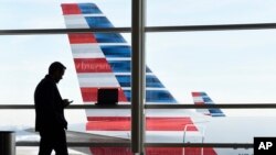 ARSIP – Seorang penumpang berbicara lewat telepon selularnya sementara sebuah pesawat American Airlines tampak diparkir di salah satu gerbang Bandara Nasional Ronald Reagan, Washington, D.C. tanggal 25 Januari 2016 (foto: AP Photo/Susan Walsh, Arsip)