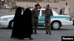 FILE - Women walk past members of Saudi security forces on patrol in Manfouha, southern Riyadh, Saudi Arabia, Nov. 14, 2013.