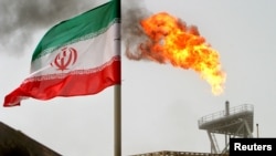 Gas suar bakar dari anjungan produksi minyak di lapangan Soroush terlihat di samping bendera Iran di Teluk Persia, Iran, 25 Juli 2005.