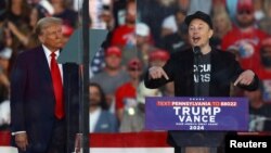 FILE - Tesla CEO and X owner Elon Musk speaks as Republican presidential nominee and former U.S. President Donald Trump looks on during a campaign rally in Butler, Pennsylvania, Oct. 5, 2024. 