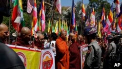 Polisi Myanmar menjaga ketat Kedutaan Thailand saat biksu dan warga Buddha melakukan aksi protes dengan memegang bendera agama dan Nasional di luar kantor tersebut, di Yangon, Myanmar, Jumat, 24 Februari, 2017. (AP Photo/Thein Zaw)
