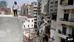 Seorang perempuan melihat dari atap ketika petugas penyelamat menggali puing-puing bangunan yang rusak parah di ibu kota Lebanon, Beirut, untuk mencari kemungkinan orang yang selamat dari ledakan besar pada bulan lalu (Foto: AFP)