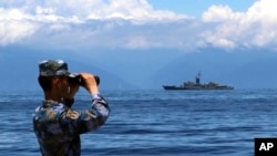 Seorang tentara China melihat melalui teropong selama latihan militer, sementara sebuah kapal fregat Taiwan "Lan Yang" terlihat di latar belakang, hari Jumat, 5 Agustus 2022.