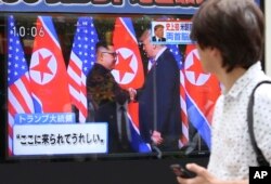 A man looks at a TV screen showing North Korean leader Kim Jong Un, left, and U.S. President Donald Trump shaking hands before their meeting in Singapore, in Tokyo, June 12, 2018. Japanese letters read: "Happy to come here."