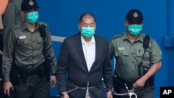 FILE - In this Dec. 12, 2020, file photo, Jimmy Lai, center, who founded the Apple Daily tabloid, is escorted by Correctional Services officers to get on a prison van before appearing in a court, in Hong Kong. 