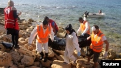 Para pekerja penyelamat membawa kantung berisi mayat seorang migran yang tersapu ke pantai di kota Janzour Tripoli, Libya (5/11). (foto: REUTERS/Hani Amara)