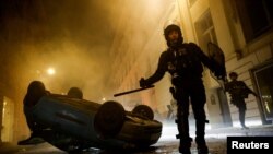 Policías antidisturbios caminan junto a un vehículo volcado por manifestantes en el 5to día de protestas en París por la muerte de un joven a manos de un agente, el 2 de julio de 2023.