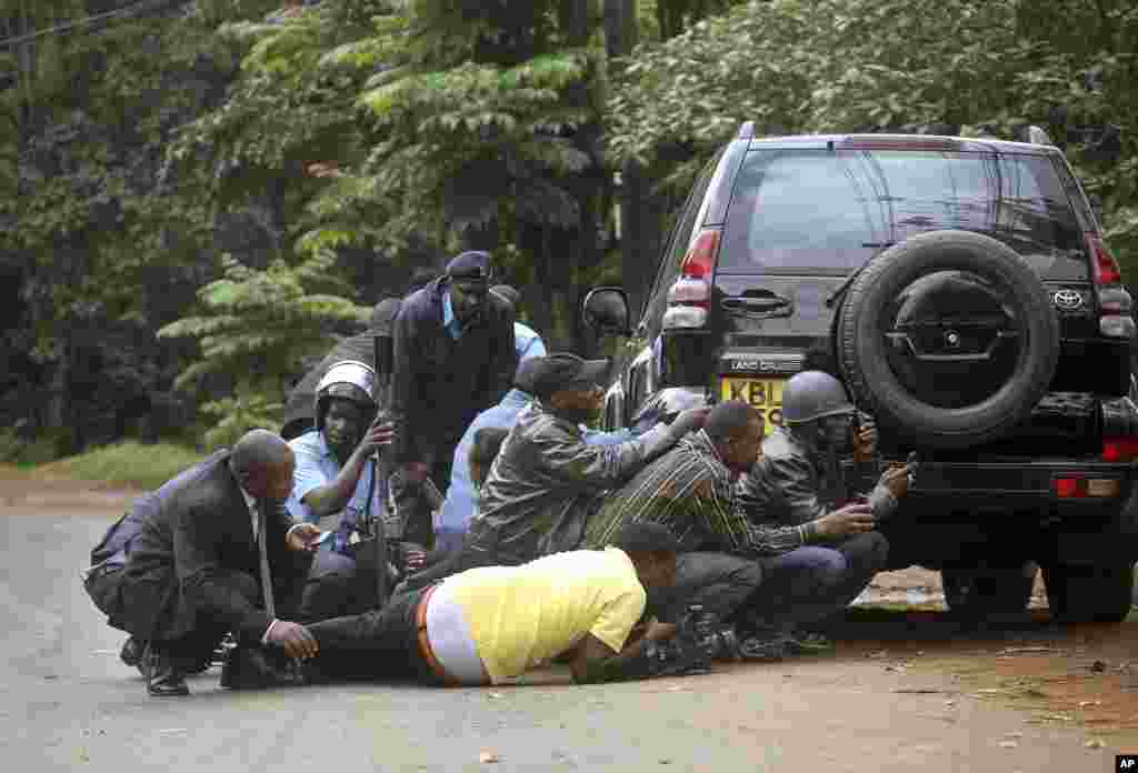 Kenyan security personnel and journalists duck behind a vehicle as heavy gunfire erupts from the Westgate Mall in Nairobi Kenya, Sept. 23, 2013. 