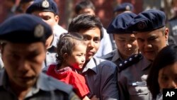 Jurnalis Reuters Kyaw Soe Oo (tengah) menggendong anak perempuannya, dikawal oleh polisi Myanmar pasca sidang pengadilan di Yangon, Myanmar (foto: dok).
