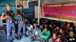 উখিয়ায় রোহিঙ্গা শরণার্থী শিবিরে হামলার পর আটক রোহিঙ্গা শরণার্থীরা নিরাপত্তা কর্মকর্তাদের পাশে বসে আছে। ২৮ অক্টোবর, ২০২২। (এএফপি ছবি/ বাংলাদেশ আর্মড পুলিশ ব্যাটালিয়ন)। ফাইল ছবি।
