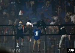 Para penonton memanjat pagar di dekat tribun penonton di tengah desak-desakan maut usai laga sepak bola antara Arema FC dan Persebaya di stadion Kanjuruhan di Malang, Jawa Timur, 1 Oktober 2022. (Foto: AFP)