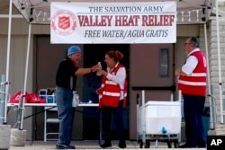 Seorang relawan memberikan air minum kepada seorang pria lansia di Stasiun Bantuan Panas pada 11 Juli 2023 di kota Phoenix, Arizona.