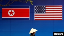 Seorang pejalan kaki melintas di depan poster bendera Korea Utara dan Amerika Serikat menjelang pertemuan Korea Utara dan AS di Hanoi, Vietnam, 25 Februari 2019. (Foto: Reuters)